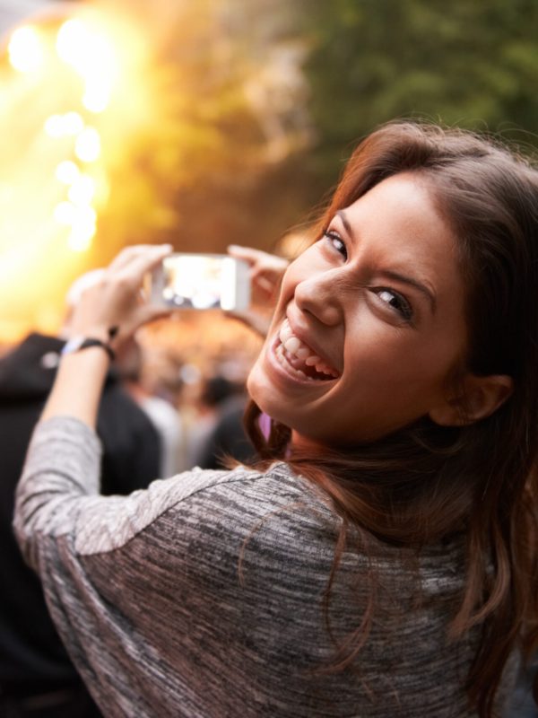 Lachende Frau filmt mit ihrem Smartphone eine Bühne